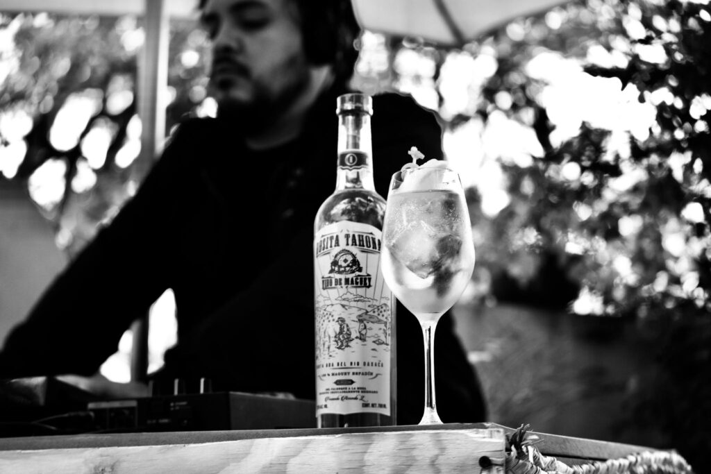 Black and white image of a DJ with a cocktail and bottle outdoors creating a lively atmosphere.