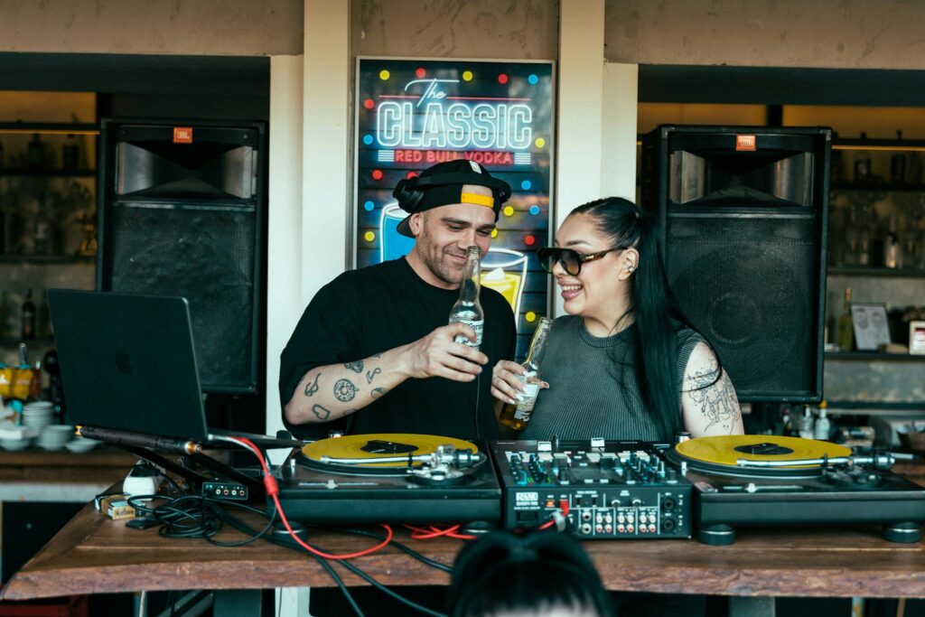 Two DJs enjoying drinks while playing music indoors with DJ equipment.